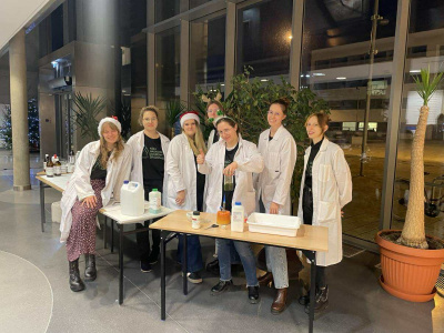 Członkowie Koła Naukowego Ochrony Środowiska podczas wydarzenia popularyzującego naukę, w fartuchach, przy stanowisku