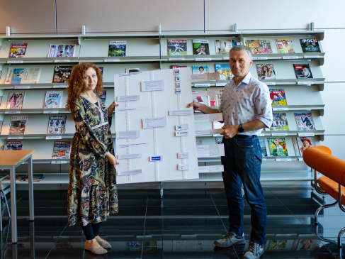 Mgr Agnieszka Wasilewska oraz mgr Zbigniew Ruszczyk trzymający  jedną z gier stworzonych przez Sekcję — tablicę, która przedstawia proces przygotowywania planu zarządzania danymi badawczymi.
