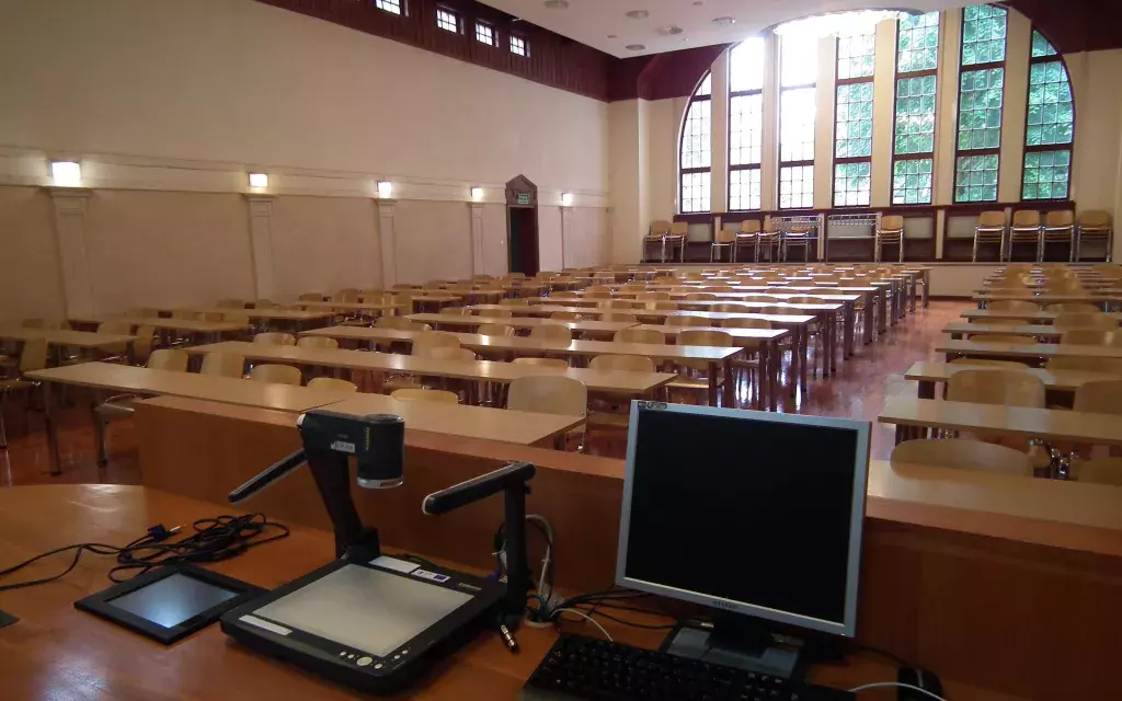 widok auli od przodu zza biurka prowadzącego. na pierwszym planie na biurku przykład wyposażenia multimedialnego :
